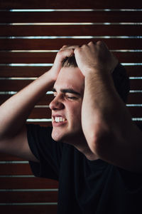 Close-up of irritated young man pulling hair by wooden wall