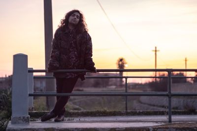 Portrait of man standing on bridge against sky during sunset