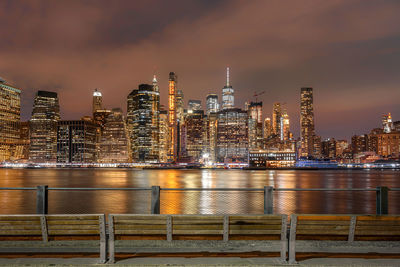 Illuminated buildings by river against sky at night