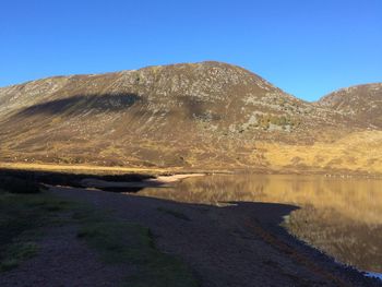 Scenic view of lake and mountains against clear blue sky