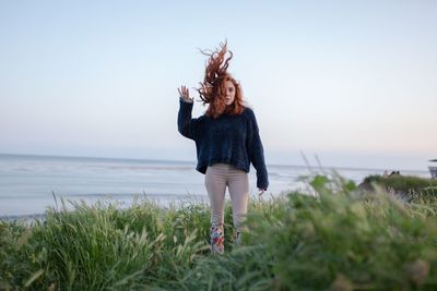 Woman with tousled hair standing on field against sky during sunset