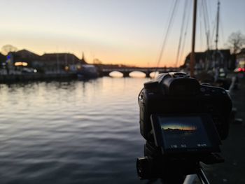 Close-up of camera on river against sky during sunset