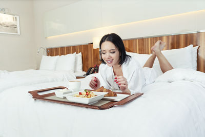 Young woman using mobile phone while sitting on bed at home