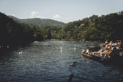 People enjoying at lake by trees against sky