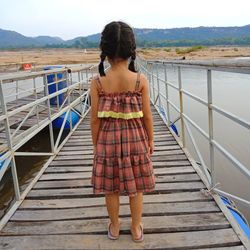 Rear view of girl standing on footbridge over sea