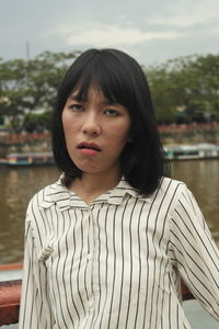 Portrait of beautiful young woman standing against lake