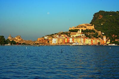 Sea by cityscape against clear blue sky