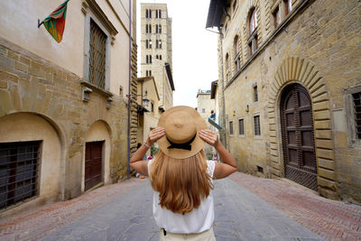 Beautiful tourist girl holds hat walking in the historic town of arezzo, tuscany, italy