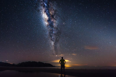 Rear view of man standing on shore while looking at milky way in sky