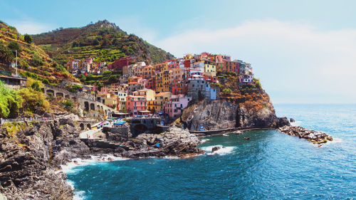 Sea by buildings on cliff against sky