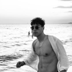 Fully unbuttoned man with sunglasses standing on beach