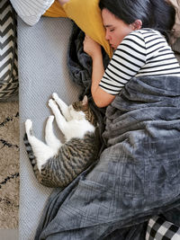 Overhead, top view of young woman and cat napping on couch. cozy, blanket, adorable, cute.