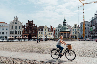 Man riding bicycle on street in city against sky