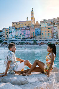 Friends sitting on water against buildings