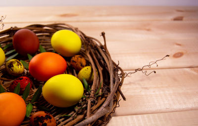 Eggs painted yellow, orange and brown lie in a nest made of wooden twigs on wooden table. 