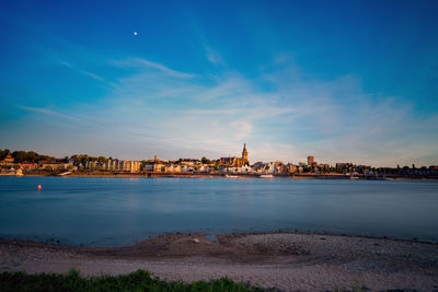 View of city at waterfront against cloudy sky