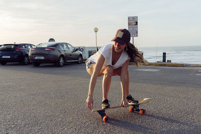 Beautiful skater practicing riding skate board on street near sea