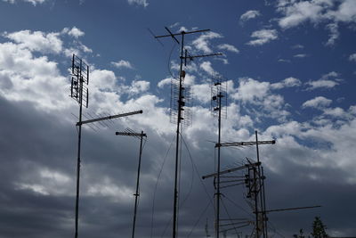 Low angle view of antennas against cloudy sky