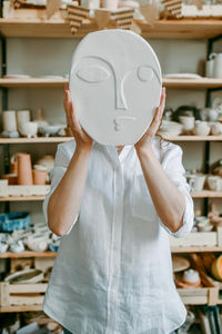 Woman hides her head behind clay product with face relief