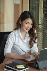 Young woman using phone while sitting on table