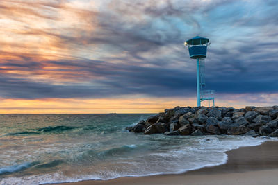 Lighthouse by sea against sky during sunset