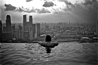 Woman swimming in infinity pool against buildings in city