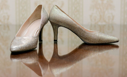 Silver high heels on glass table with reflection