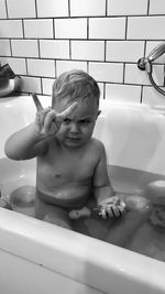 Cute boy gesturing horn sign while sitting in bathtub at home