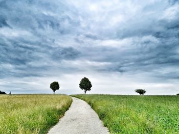 Empty road amidst field against sky