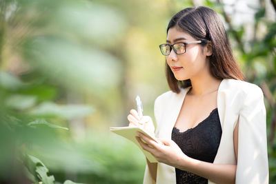 Portrait of young woman holding eyeglasses standing outdoors