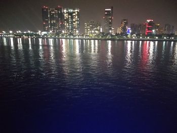 Illuminated buildings by sea against sky at night