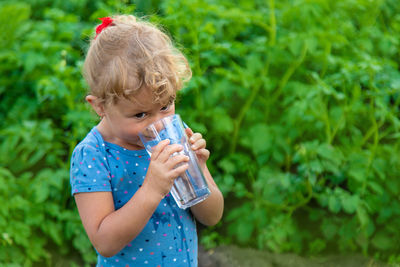 Young woman drinking water while standing against plants