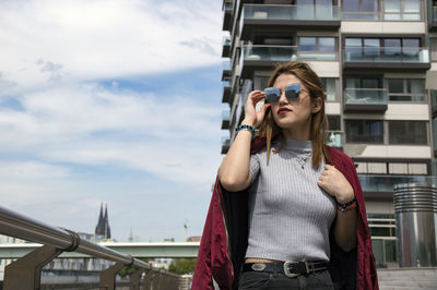 Young woman standing by railing against sky in city