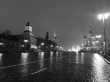 Illuminated buildings by river against sky in city at night