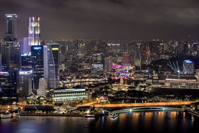 Illuminated buildings by river against sky in city at night