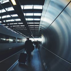 Rear view of man pulling wheeled luggage by train at station