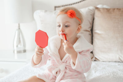 Cute girl applying make-up while sitting on bed at home