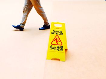 Low section of man walking by caution wet floor sign