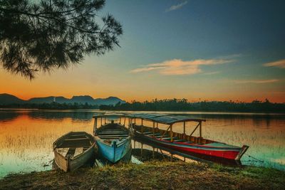 Boat moored on shore against sky during sunset