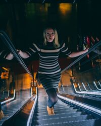 Full length portrait of young woman standing on escalator