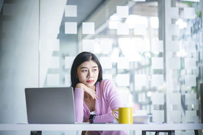 Portrait of young woman using phone while sitting on table