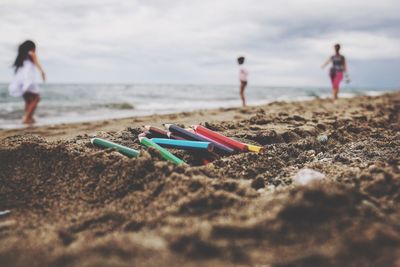 Close-up of colored pencils on sand against people at beach