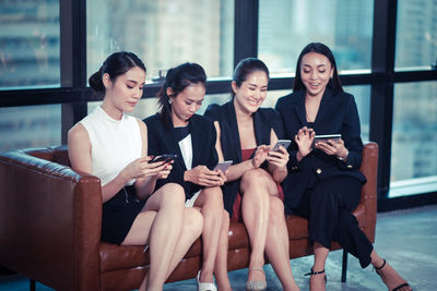 Young woman using phone while sitting on laptop