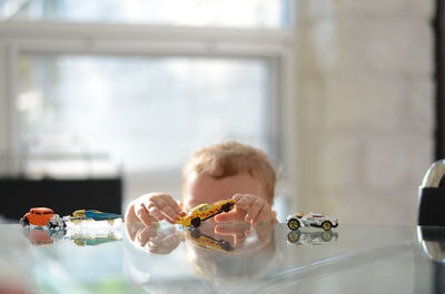 Portrait of toddler boy playing with cars ontop of glass table