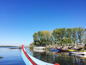 Boats moored in river against clear blue sky