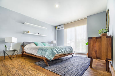 Bed base, bedroom with mat on the floor, clay pot in the background, wooden credenza and mirror.