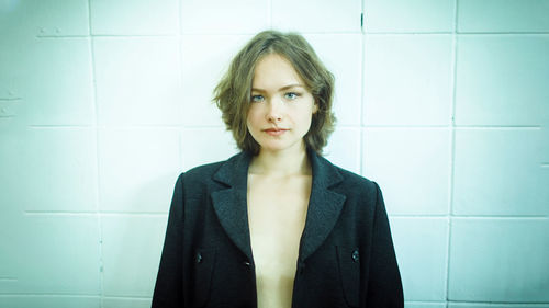 Portrait of young woman standing against wall