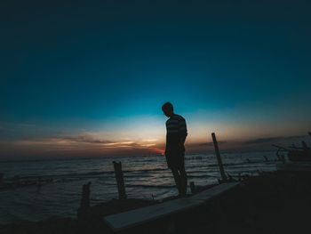 Silhouette man looking at sea against sky during sunset