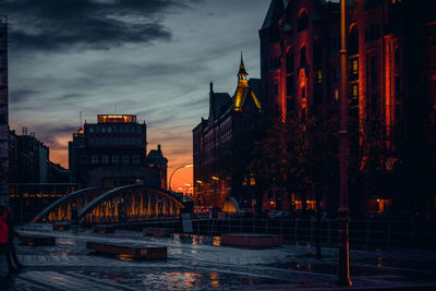 Bridge over river amidst buildings in city at sunset