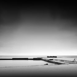 Pier at beach against sky during foggy weather